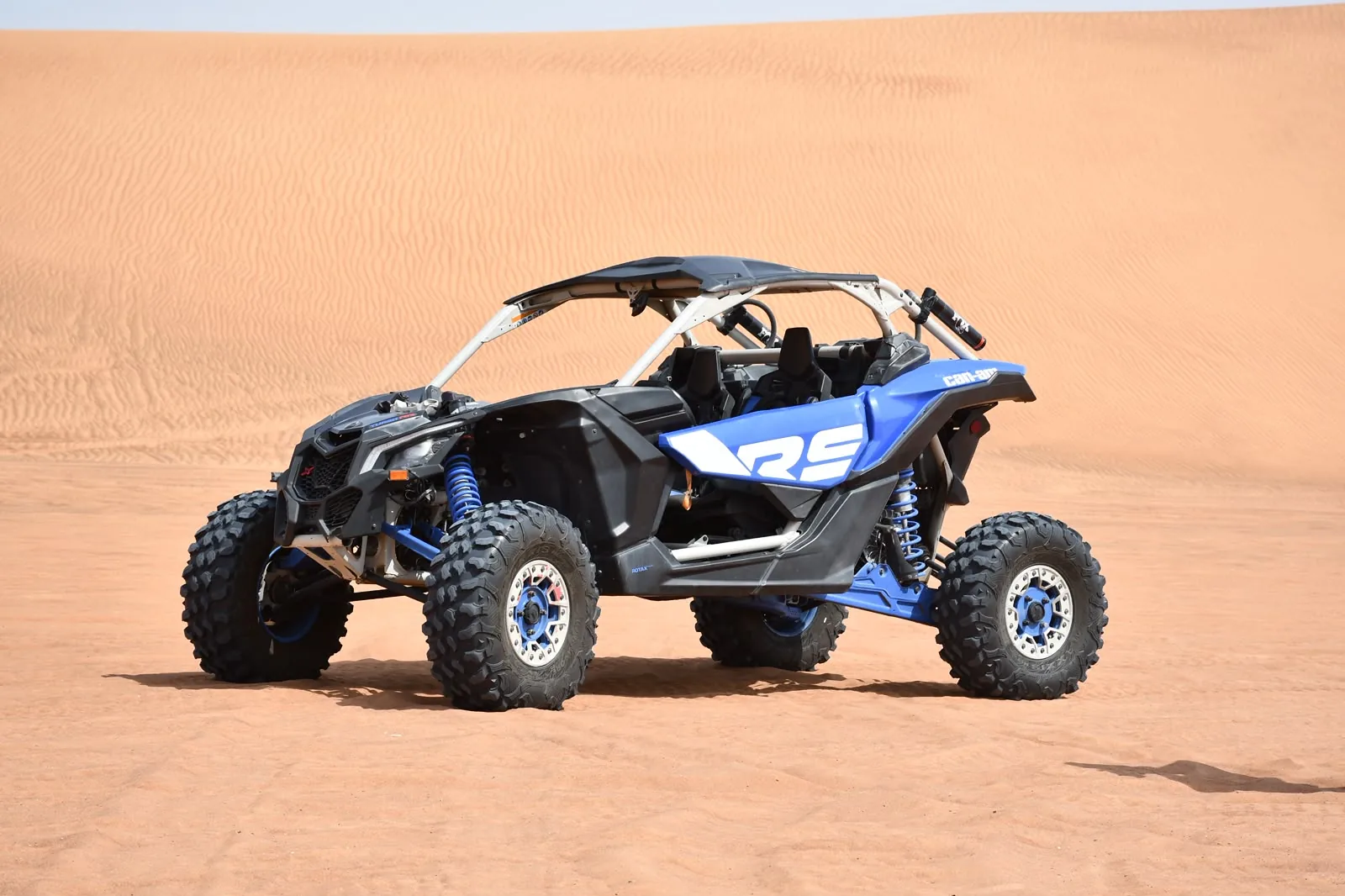 Blue Can-Am Maverick R dune buggy parked on Dubai desert sand