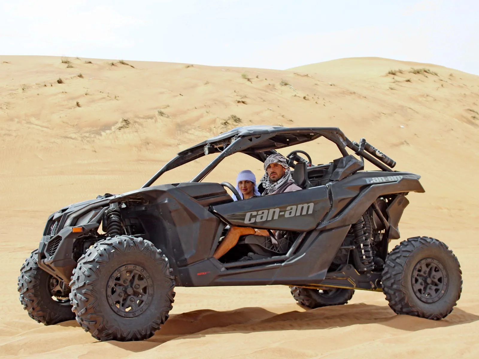 Two guests in a Can-Am Maverick X3 two seater below a Lahbab red dune in Dubai