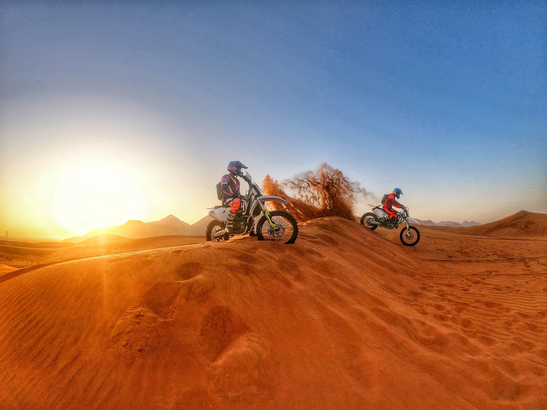 KTM dirt bike riders climbing a dune at sunrise in the Dubai desert