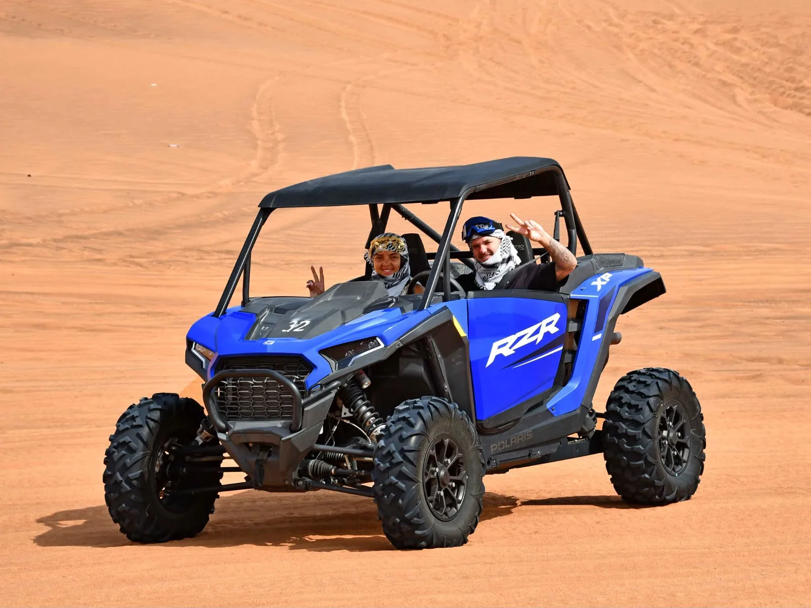 Two riders in a blue Polaris RZR 1000 two seater on the Lahbab red dunes in Dubai