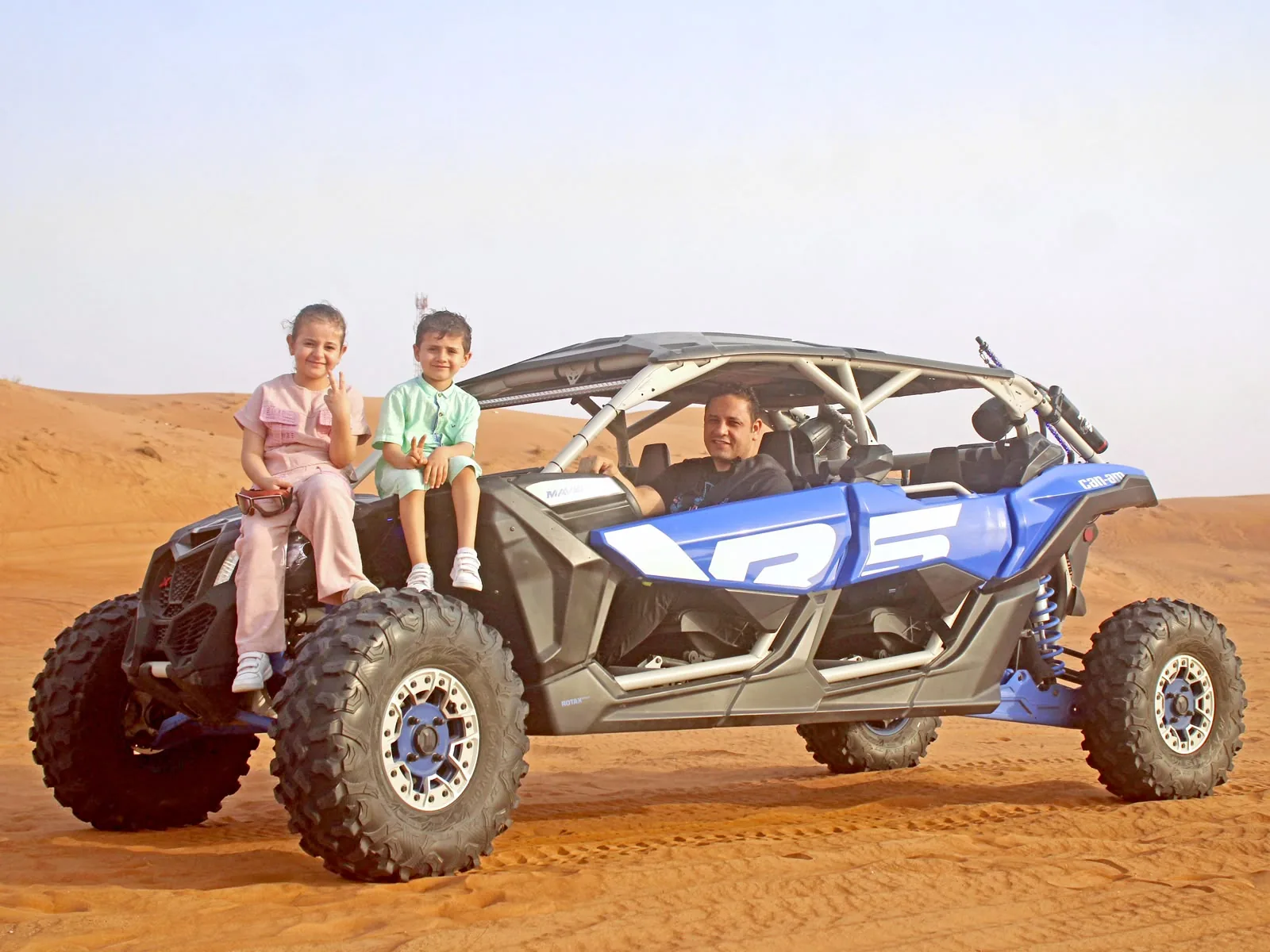 Two children sitting on the front of a dune buggy in the Dubai desert