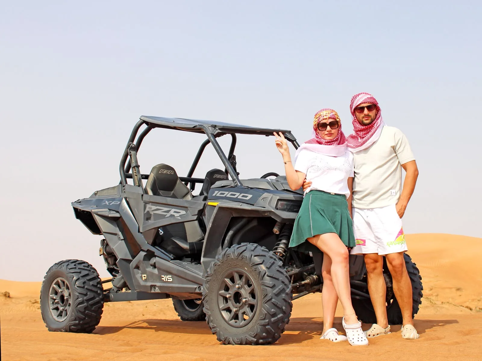 Couple standing beside a Polaris RZR dune buggy in the Dubai desert