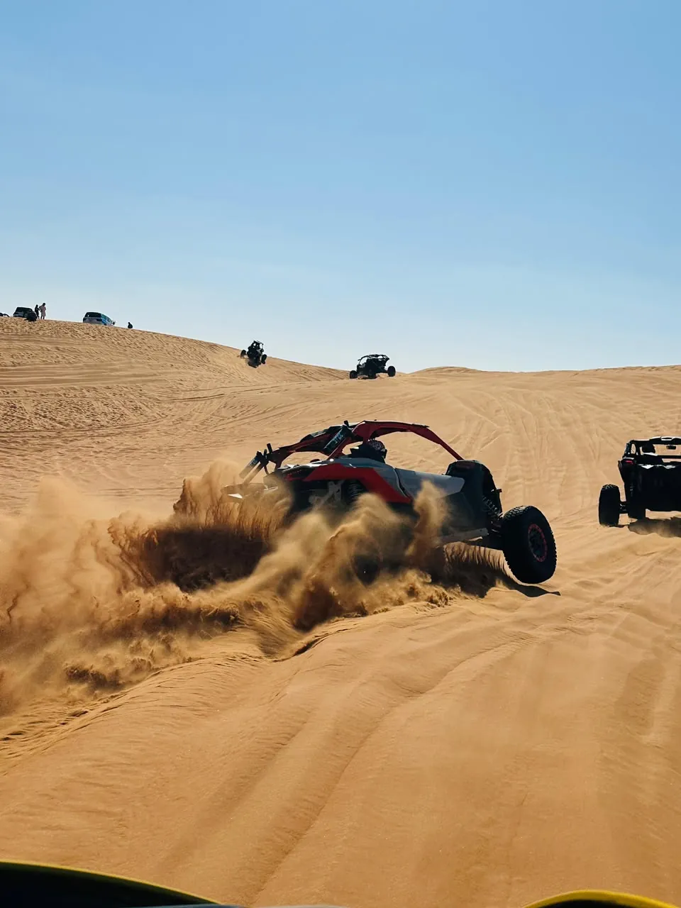 Dune buggy climbing a red dune in convoy during a Dubai desert tour