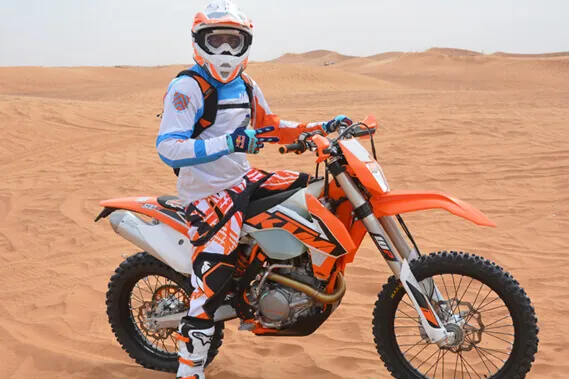 Rider standing with a KTM 450 dirt bike on a Dubai desert dune