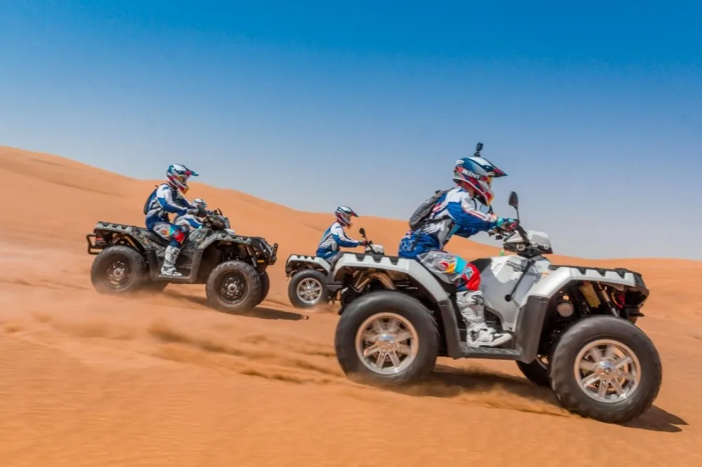 Three riders on single seat quad bikes climbing a red dune in the Dubai open desert